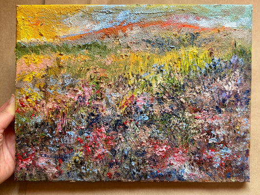 Hand holding a small oil painting of a landscape with colorful brushstrokes.